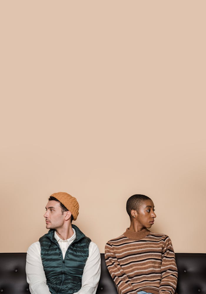 gallery-6 Multiethnic couple looking in opposite ways while sitting on leather sofa on beige background